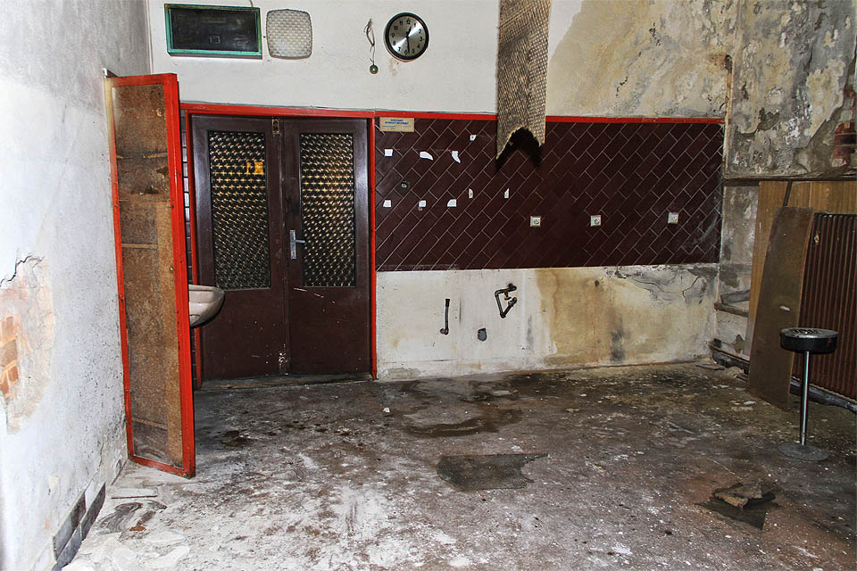 Dveře s falešným terčíkovým sklem, popelník, eleganterózní hodiny a výzdoba stěn prozrazují, že v tomhle zavlhlém podzemí byl v 90. letech 20. století nejspíš bar.