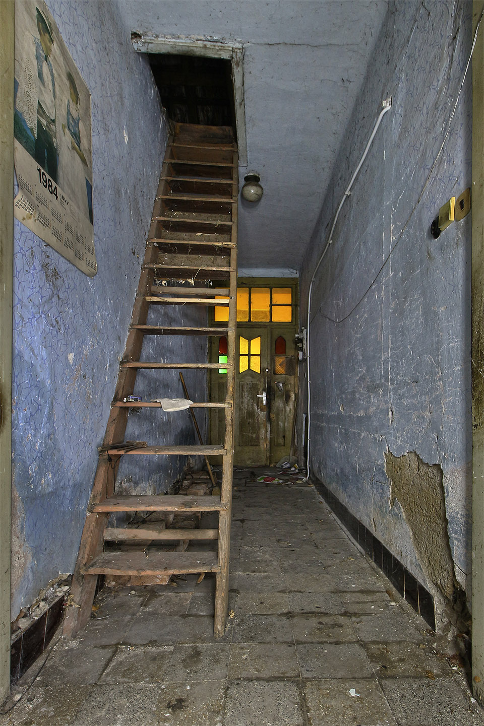 V úzké chodbě se nacházejí pouze schody na půdu a kalendář z roku 1984.