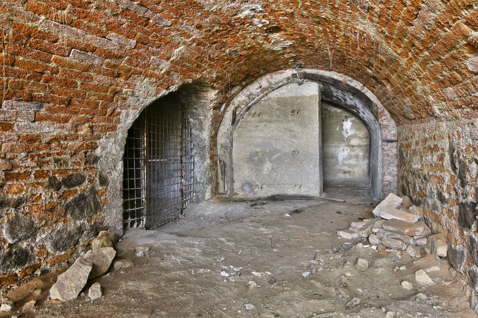 Sklep začíná dvojicí masivních betonových stěn, které tvoří protitlakovou zábranu pro případ exploze bomby v prostoru domu nebo bezprostředně před ním. Jde zřejmě o úpravu z doby 2. světové války, kdy sloužily prostory jako kryt, přesto, že sklep sám může být možná až o dvě století starší. Jako nouzové východy zde sloužily dvě chodby spojující sklep s podzemím sousedních domů. Vlevo je na fotce vidět branka, která brání přístupu do větší místnosti, spojené úzkou chodbičkou se sklepy domu č. 60.